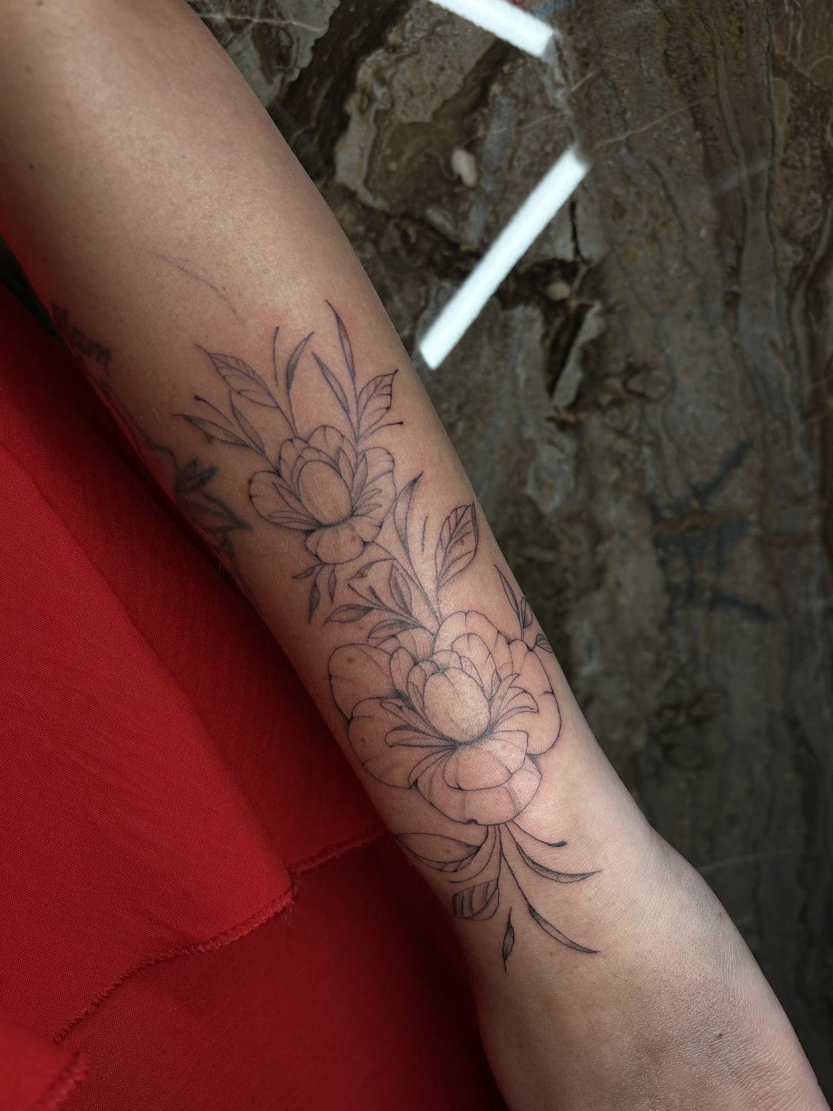 Fine-line tattoo van een pioenroos op de onderarm
